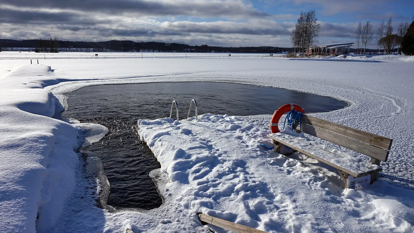 Ice hole for winter swimming in a frozen lake at Peurunka, Finland, with a ladder, a life ring and a bench in the snow