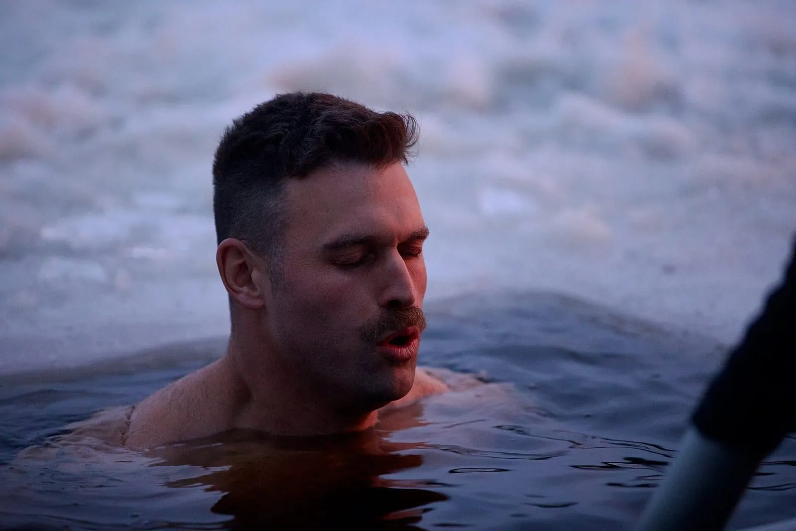 Man with eyes closed submerged to the shoulders in an ice hole, during a winter swim in Finland