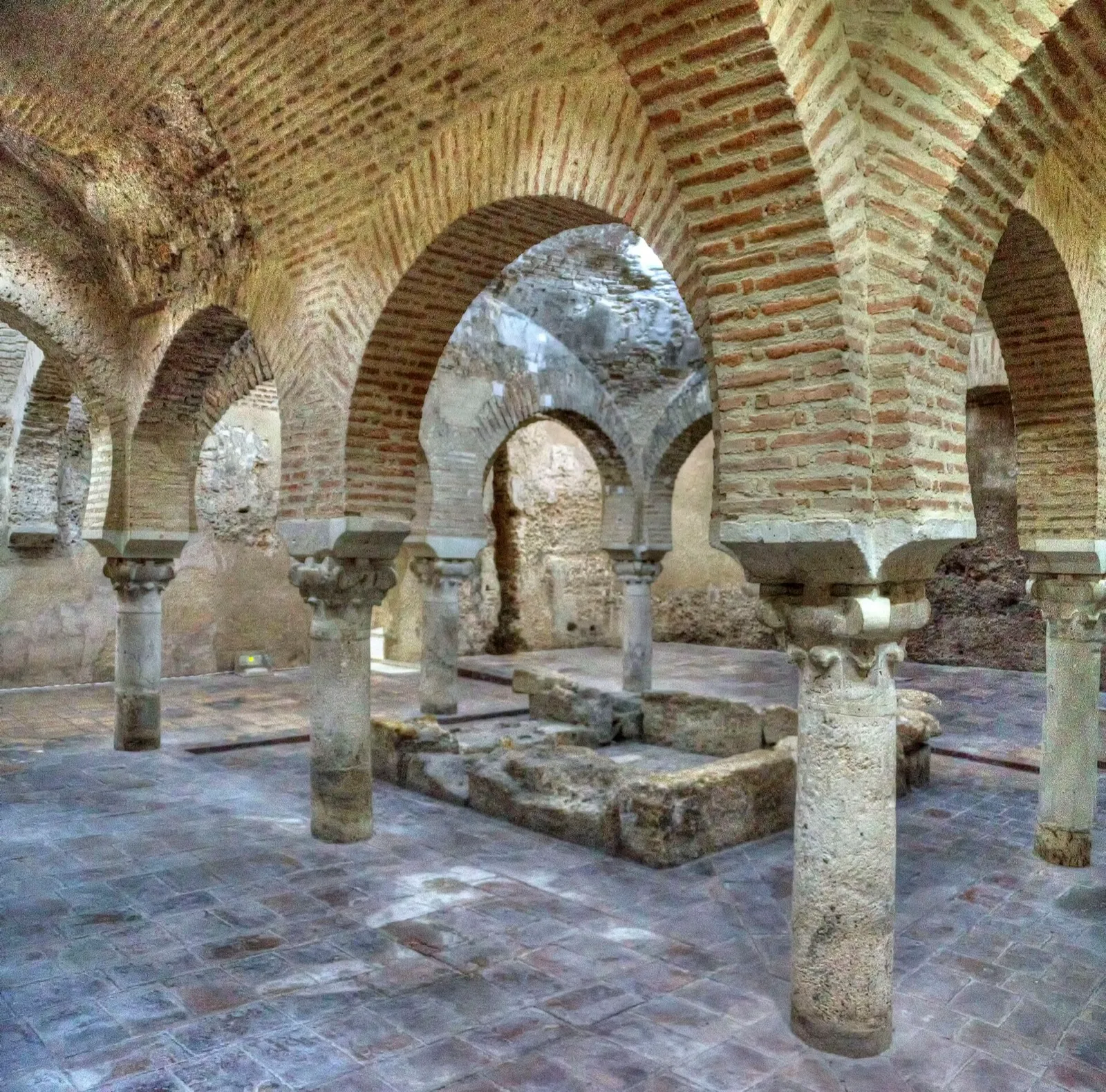 Central room of the Arab baths of Jaén, with brick horseshoe arches on stone columns and a basin in the middle