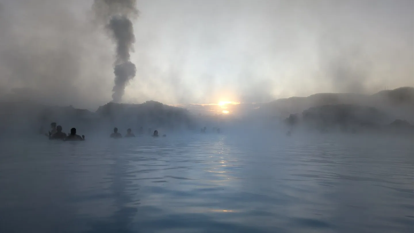 Sunrise at the Blue Lagoon in Iceland, with steam over the milky blue water and bathers in the distance