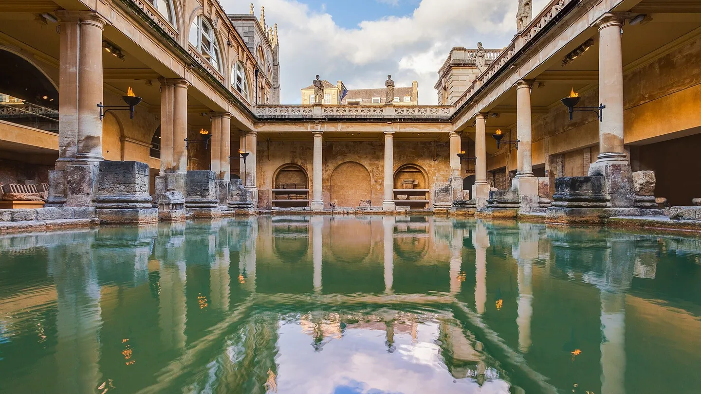 The Great Bath of the Roman Baths at Bath, England, its green pool ringed by columns and the nineteenth-century upper terrace