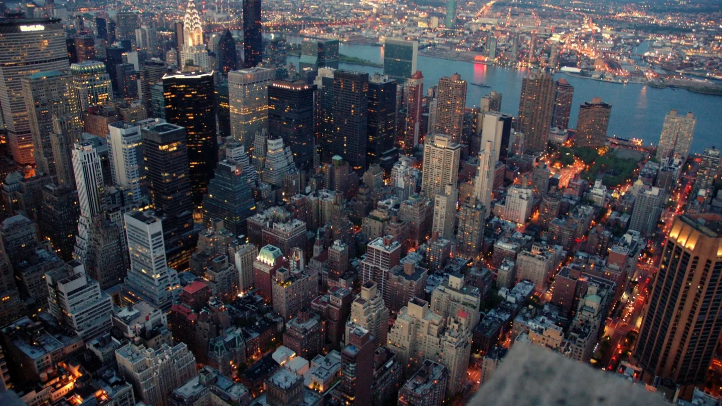 Manhattan seen from above at dusk, with the Midtown buildings lit up and the East River behind