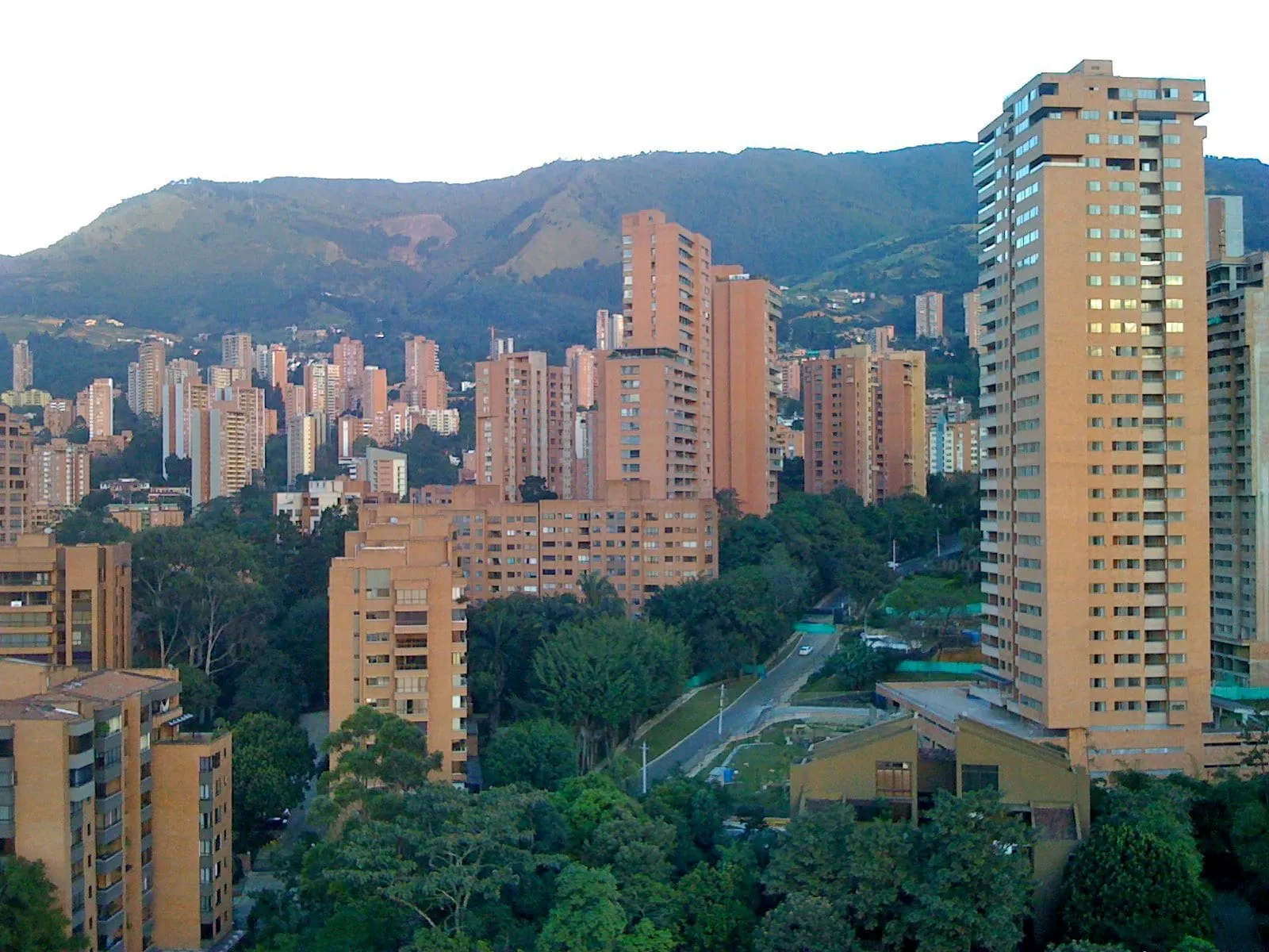 View of El Poblado in Medellín, with brick towers among trees and the mountains behind