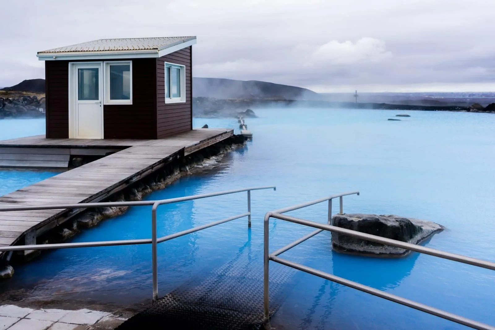 Turquoise lagoon of the Mývatn Nature Baths, with a wooden deck, a railing and steam over the water