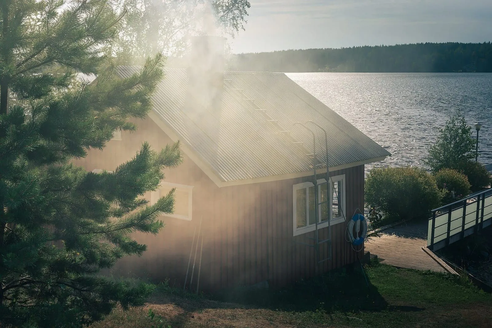 Smoke rising from the chimney of a timber sauna by a lake in Finland, among pines