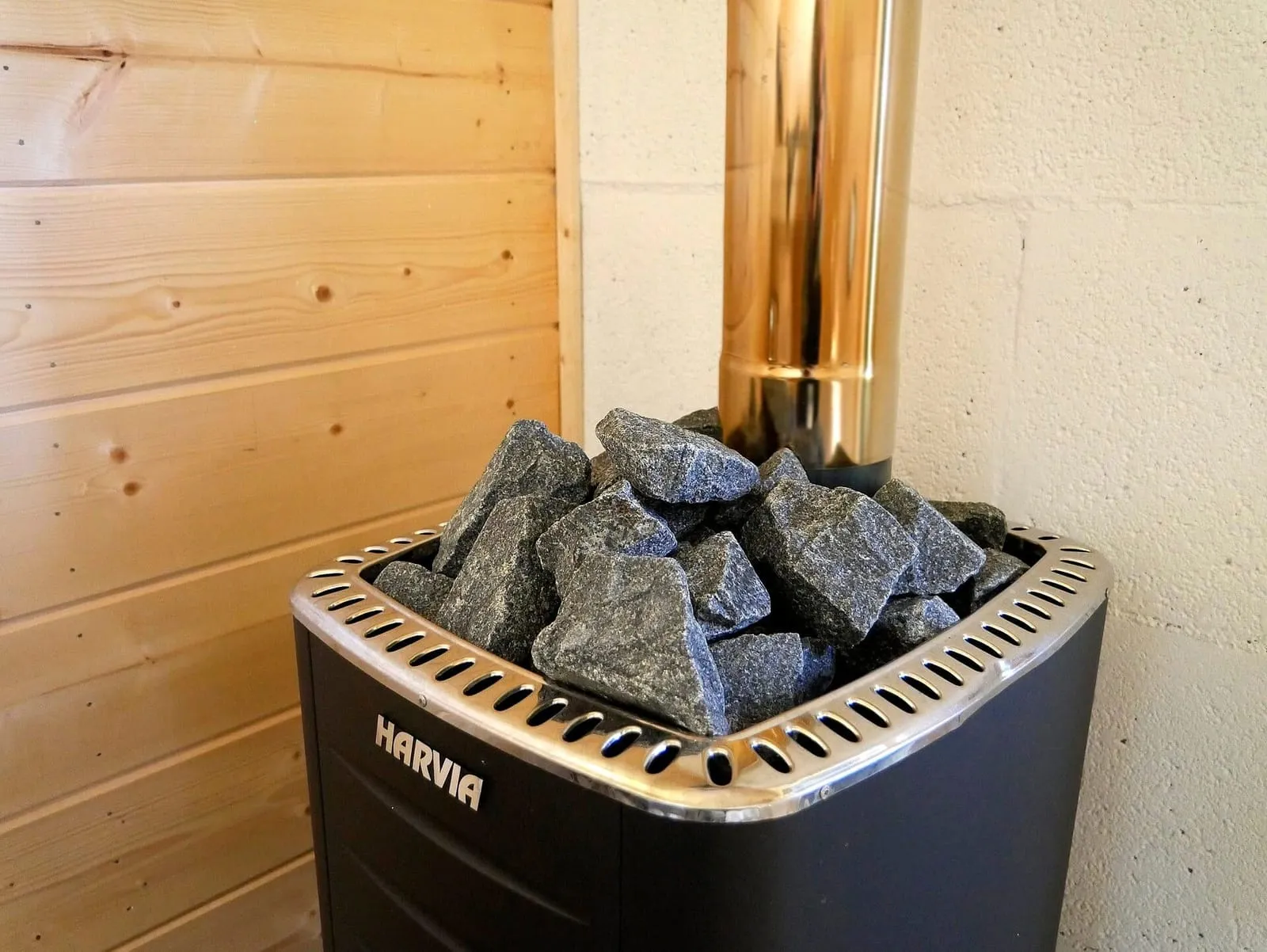 Black electric sauna heater with stones on top, in the corner of a pale-wood sauna