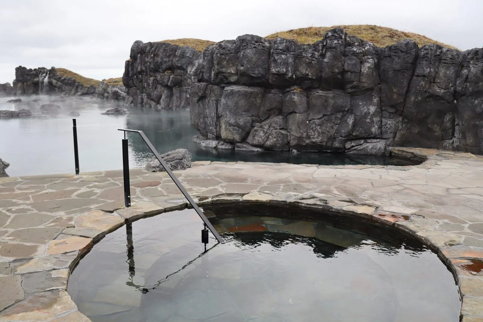 Round stone cold plunge at Sky Lagoon, with basalt walls and the geothermal lagoon behind