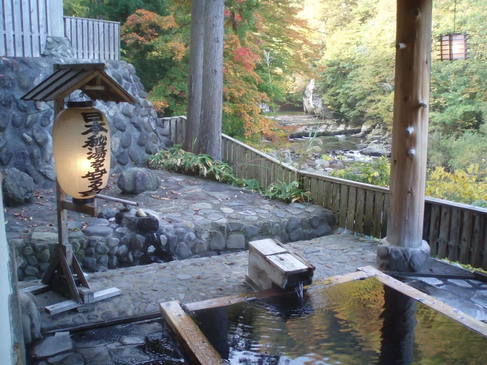 Outdoor stone bath at Takanoyu Onsen in Akita, among trees and a wooden lantern
