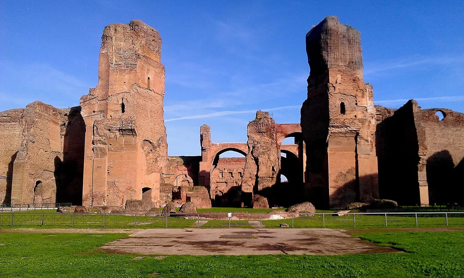 Brick ruins of the Baths of Caracalla in Rome, tall walls and arches seen from the lawn towards the caldarium